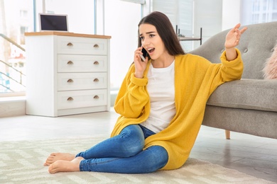 Photo of Young woman talking on mobile phone near sofa