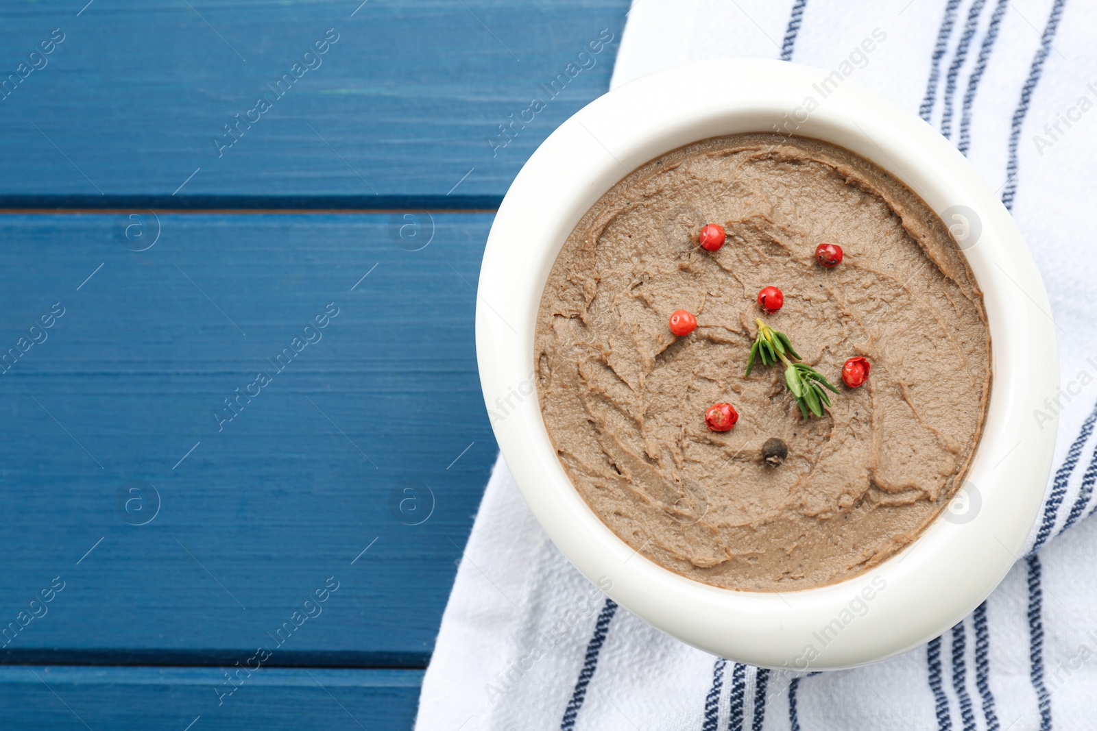 Photo of Tasty liver pate with pepper and herb in bowl on blue wooden table, top view. Space for text