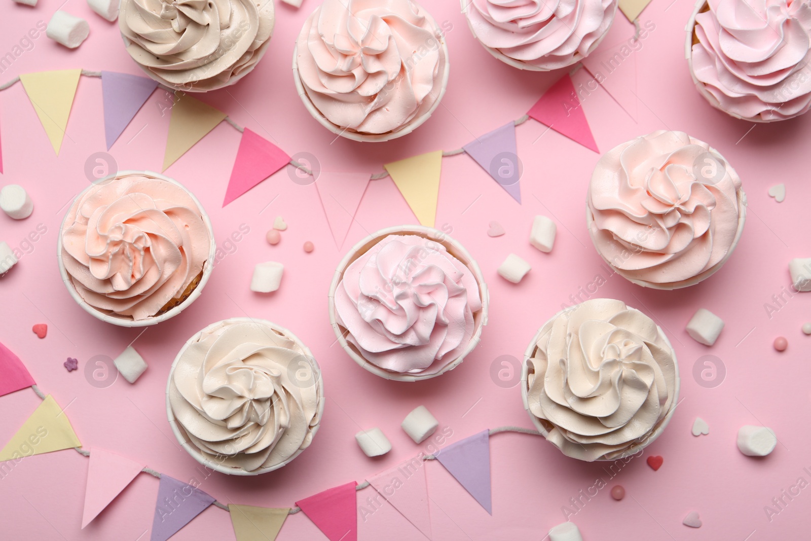 Photo of Delicious birthday cupcakes, bunting flags, marshmallows and sprinkles on pink background, flat lay