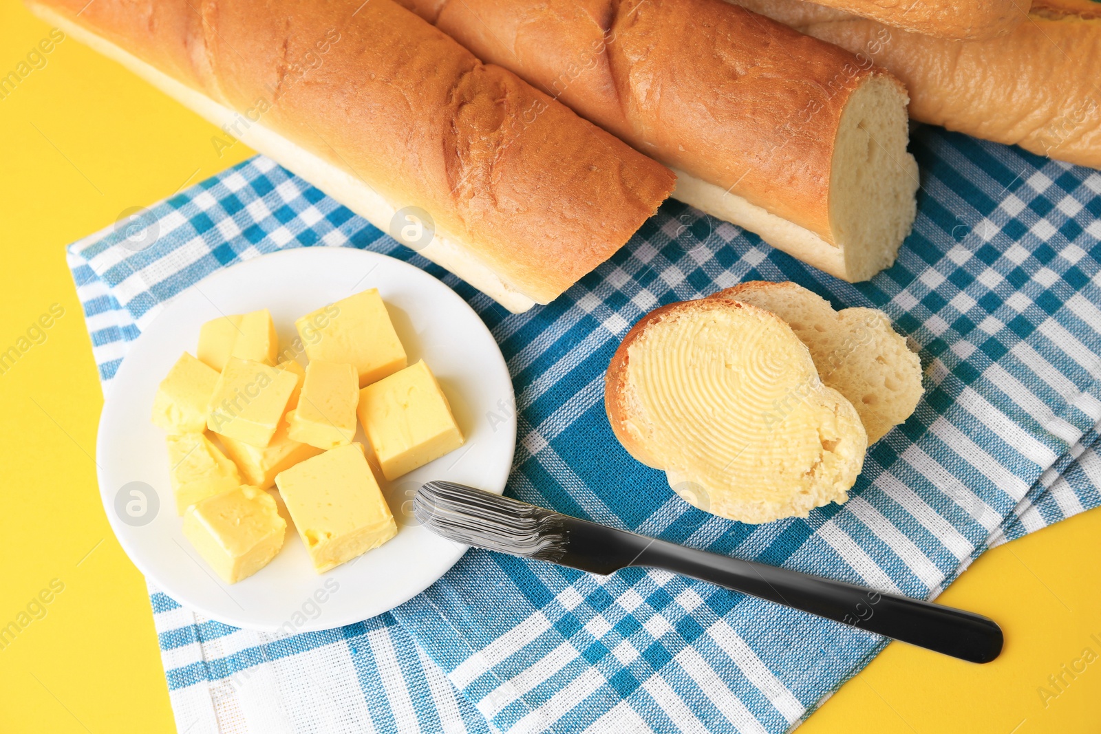 Photo of Cut baguette with fresh butter on yellow background, above view