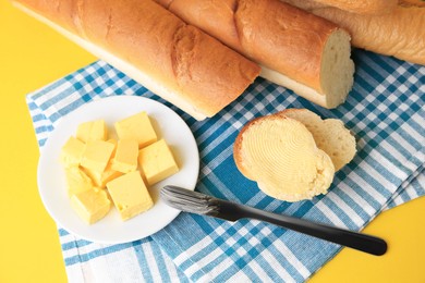 Photo of Cut baguette with fresh butter on yellow background, above view