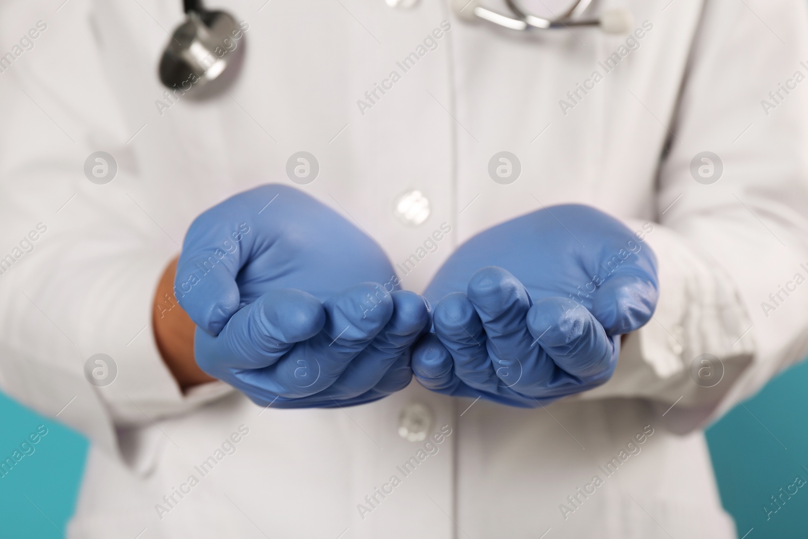 Photo of Doctor with stethoscope holding something on light blue background, closeup. Cardiology concept