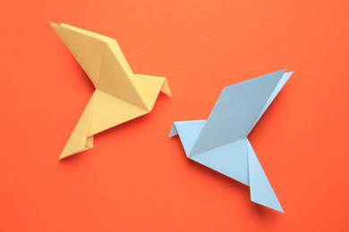 Photo of Beautiful colorful origami birds on orange background, flat lay