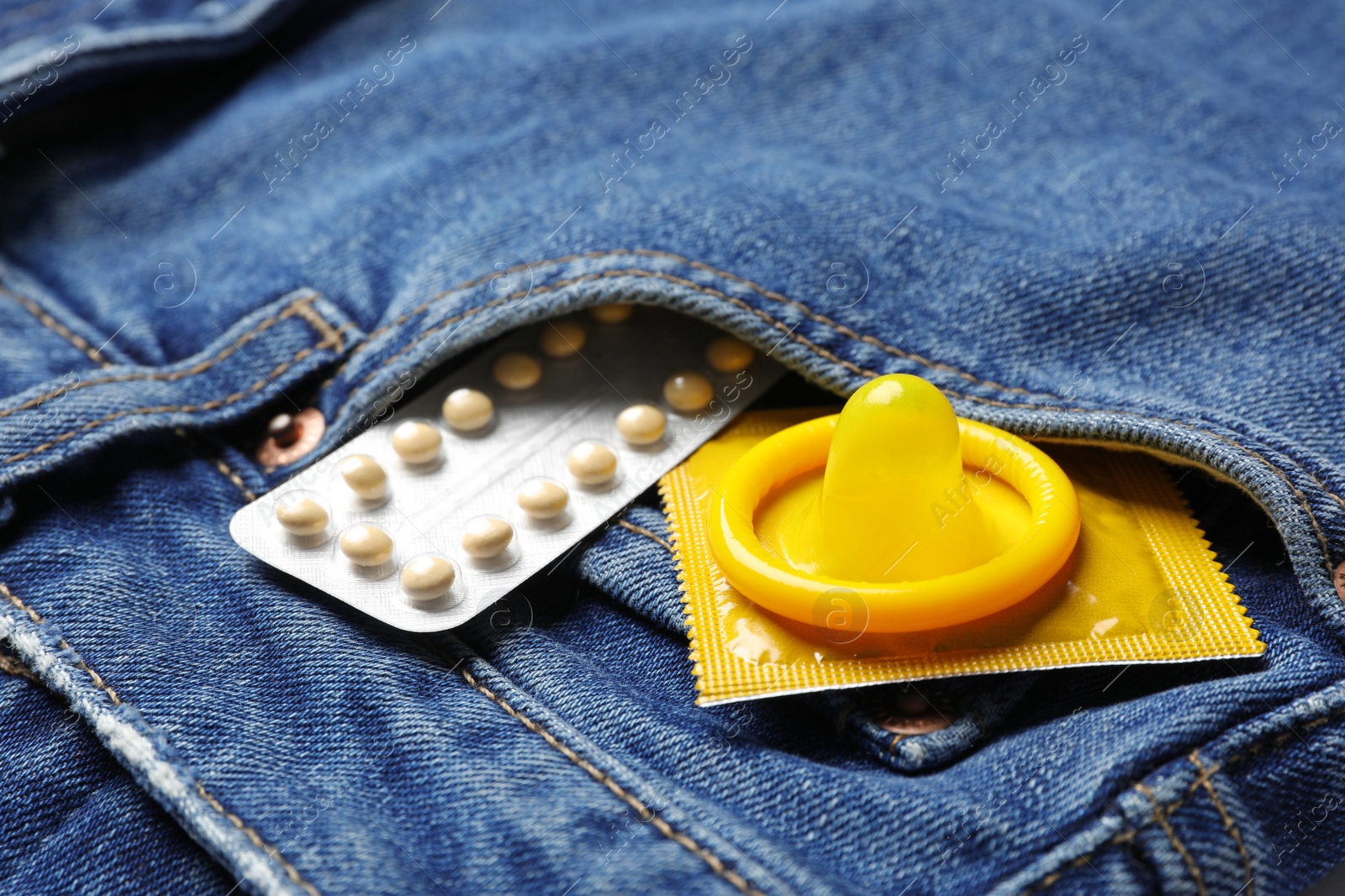 Photo of Yellow condoms and birth control pills in pocket of jeans, closeup. Safe sex concept