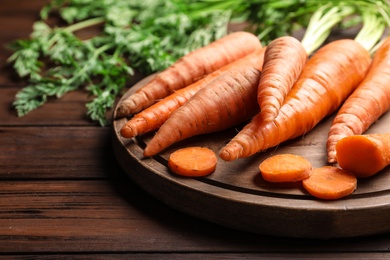 Board with fresh carrots on wooden background, closeup. Space for text