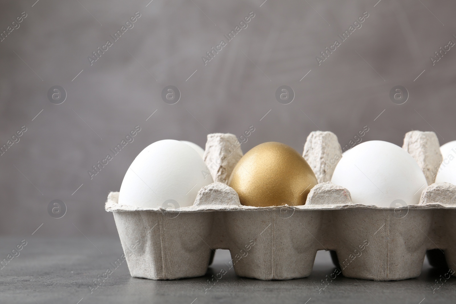 Photo of Carton with golden egg and others on grey background