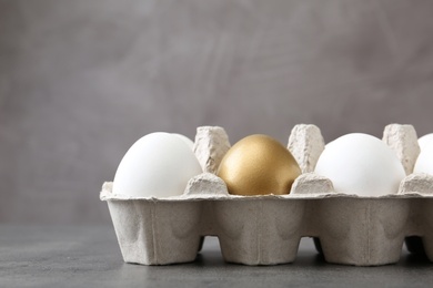 Carton with golden egg and others on grey background