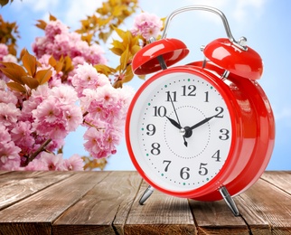 Image of Red alarm clock on wooden table. Daylight saving time (Spring forward)