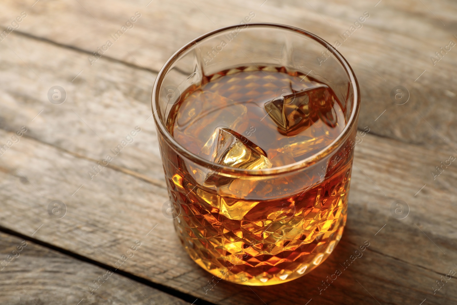 Photo of Golden whiskey in glass with ice cubes on wooden table