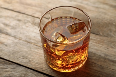 Golden whiskey in glass with ice cubes on wooden table