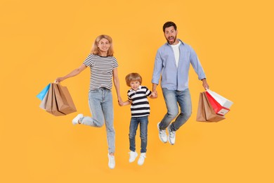 Family shopping. Happy parents and son jumping with paper bags on orange background