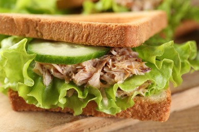 Photo of Delicious sandwich with tuna, cucumber and lettuce leaves on wooden board, closeup