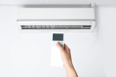 Photo of Woman operating air conditioner with remote control indoors, closeup