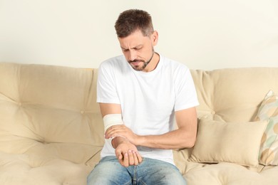 Photo of Man with arm wrapped in medical bandage on sofa indoors