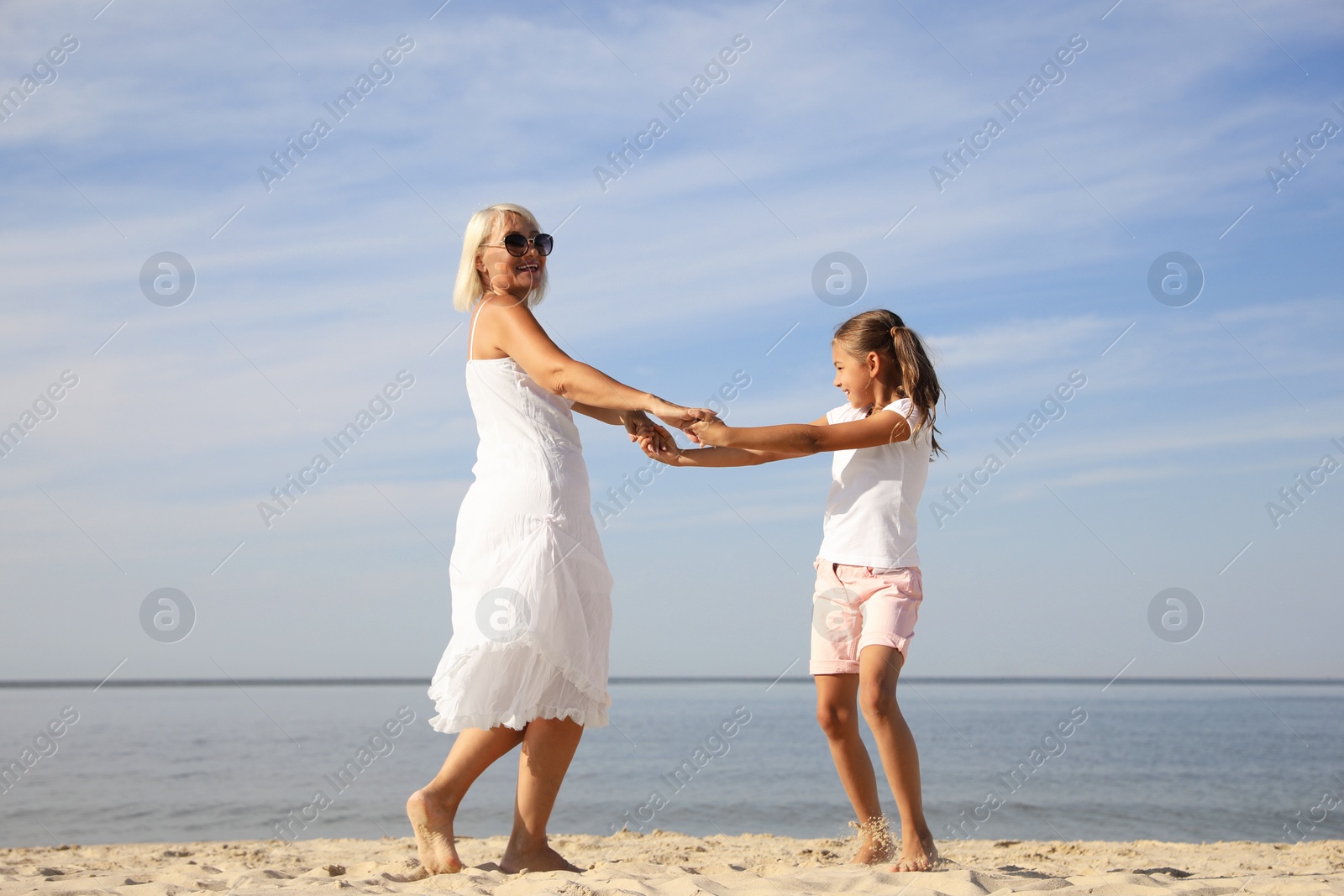 Photo of Cute little girl with grandmother spending time together on sea beach