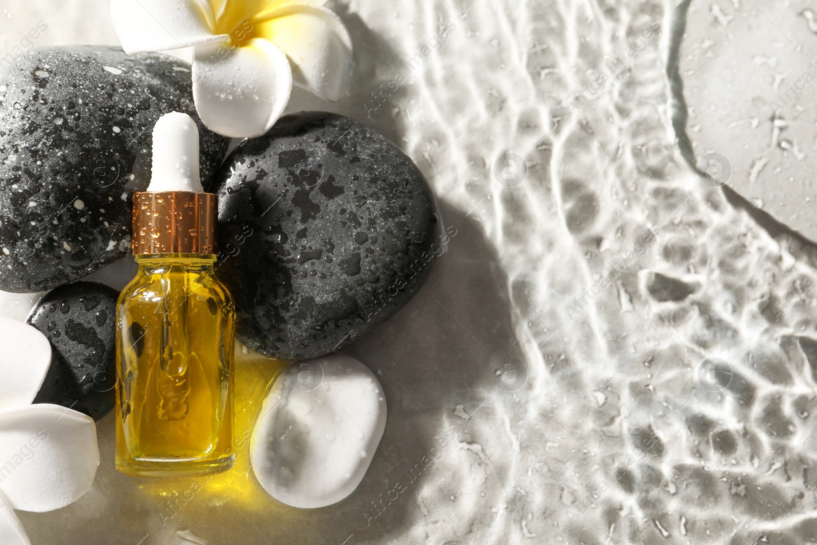 Photo of Bottle of face serum and spa stones in water on light background, flat lay. Space for text