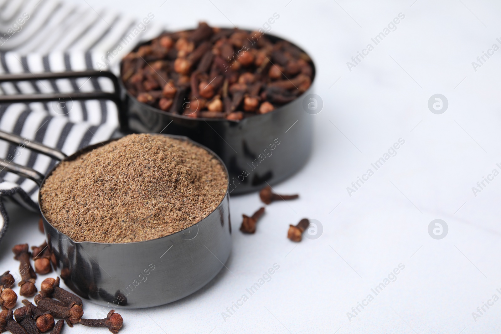 Photo of Aromatic clove powder and dried buds in scoops on white table, closeup. Space for text