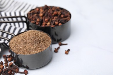 Aromatic clove powder and dried buds in scoops on white table, closeup. Space for text