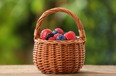 Photo of Wicker basket with different fresh ripe berries on wooden table outdoors