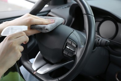 Woman cleaning steering wheel with rag in car, closeup