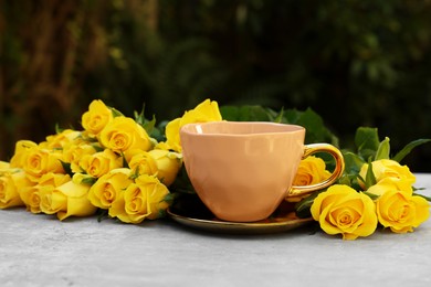 Cup of drink and beautiful yellow roses on light table outdoors