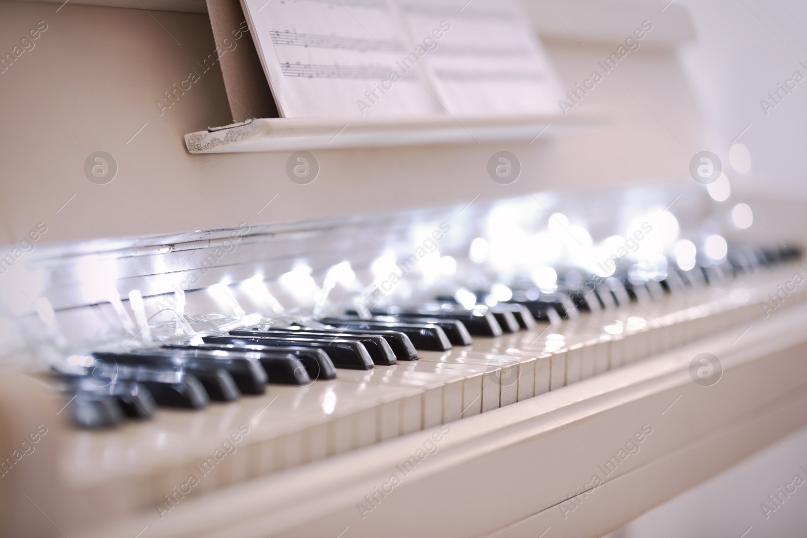 Photo of Glowing fairy lights on piano keys, closeup. Christmas music