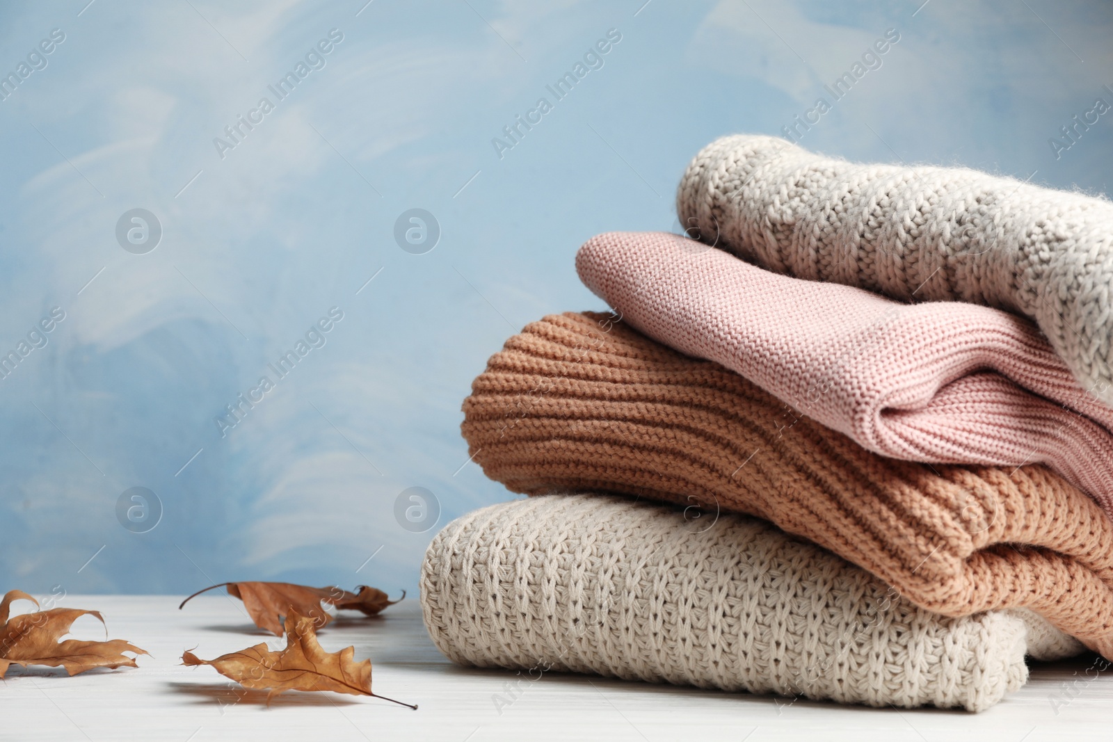 Photo of Stack of folded knitted sweaters and autumn leaves on table. Space for text