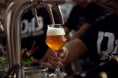 Bartender pouring beer into glass in pub, closeup