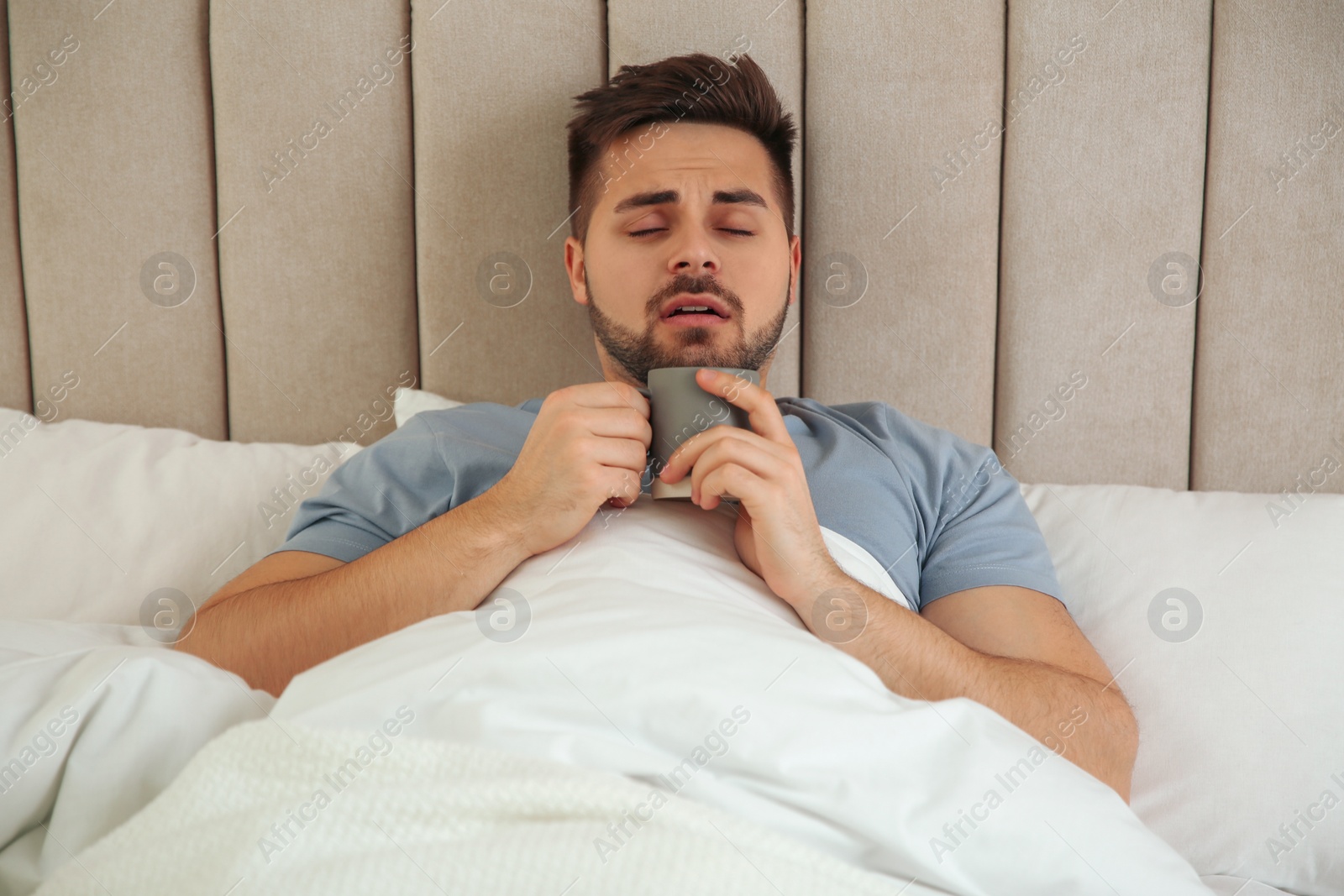 Photo of Sick young man with cup of hot drink in bed at home. Influenza virus