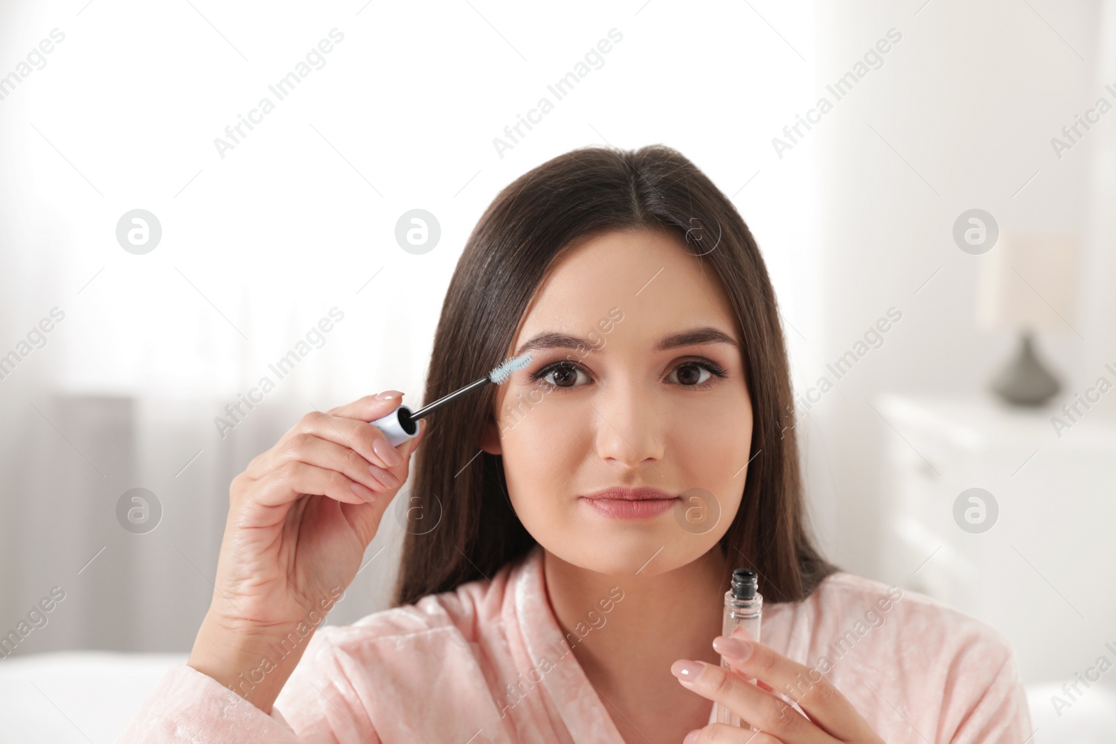 Photo of Beautiful woman applying oil onto her eyelashes indoors