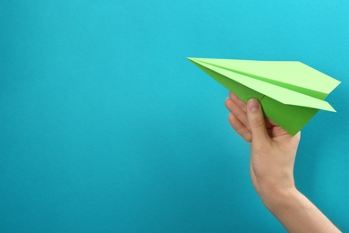 Woman holding paper plane on light blue background, closeup. Space for text