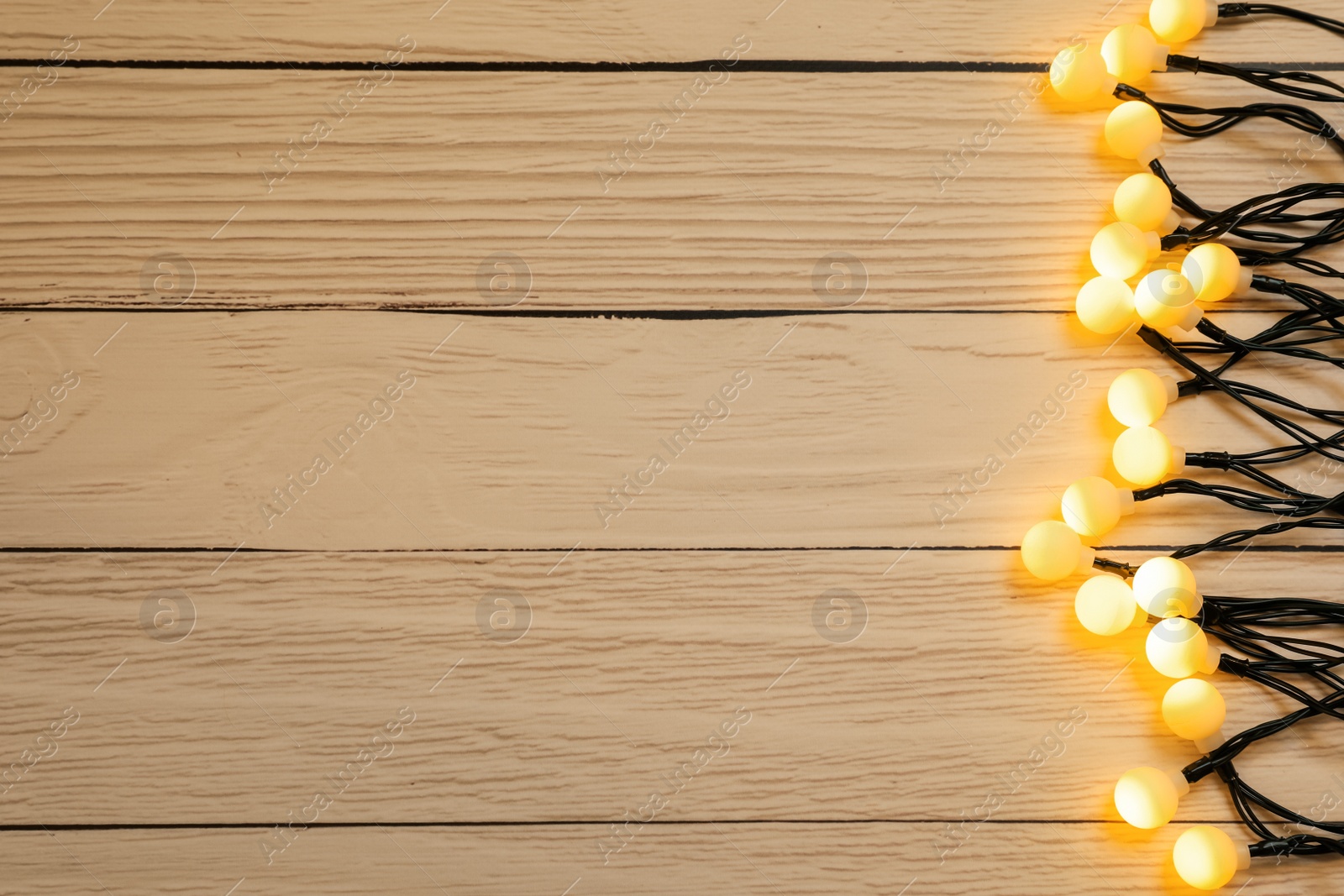 Photo of Glowing festive lights on wooden background, top view. Space for text