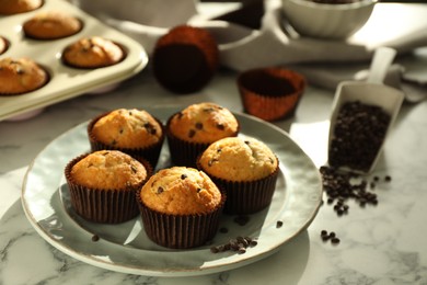 Photo of Delicious sweet muffins with chocolate chips on white marble table