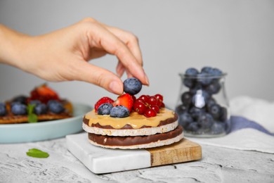 Photo of Woman decorating crunchy rice cakes with blueberry at white textured table, closeup