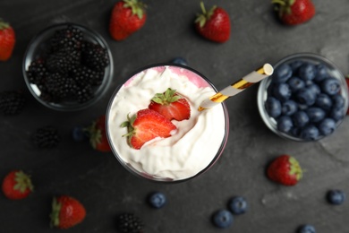 Photo of Tasty milk shake with whipped cream and fresh berries on black slate table, flat lay