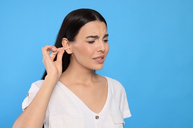 Young woman cleaning ear with cotton swab on light blue background. Space for text