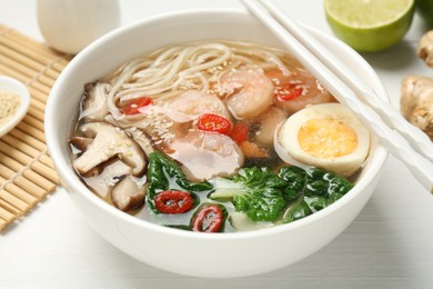 Tasty ramen with shrimps in bowl and chopsticks on white table, closeup