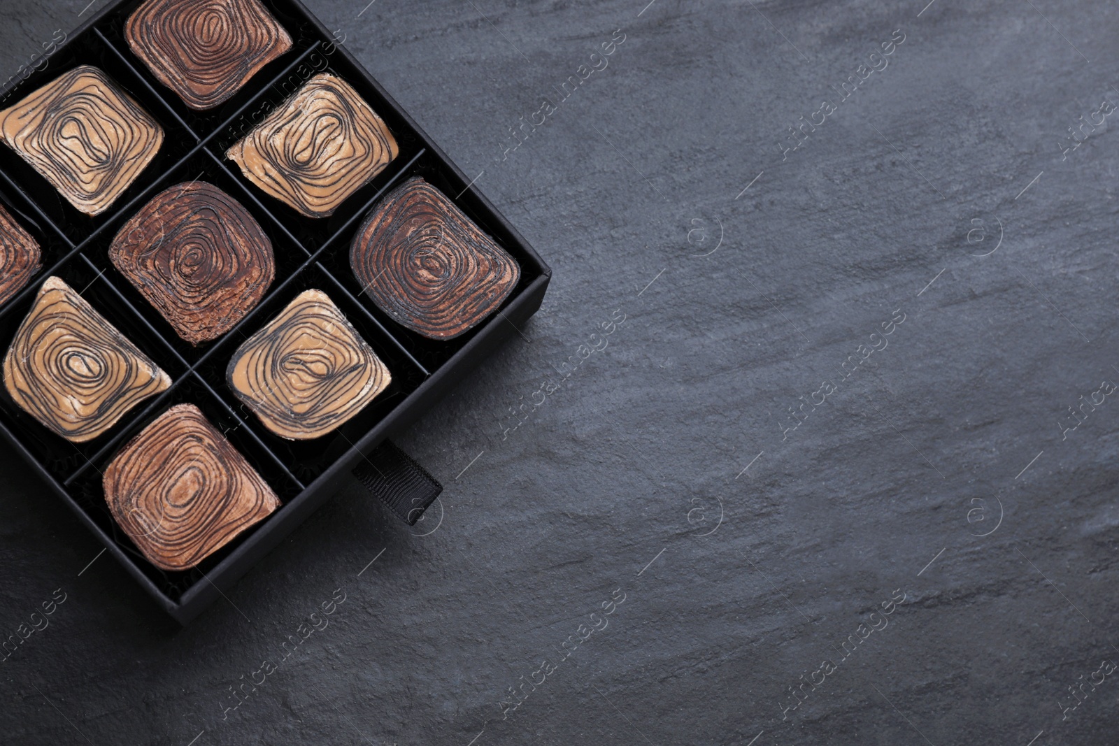 Photo of Box of tasty chocolate candies on black table, top view. Space for text