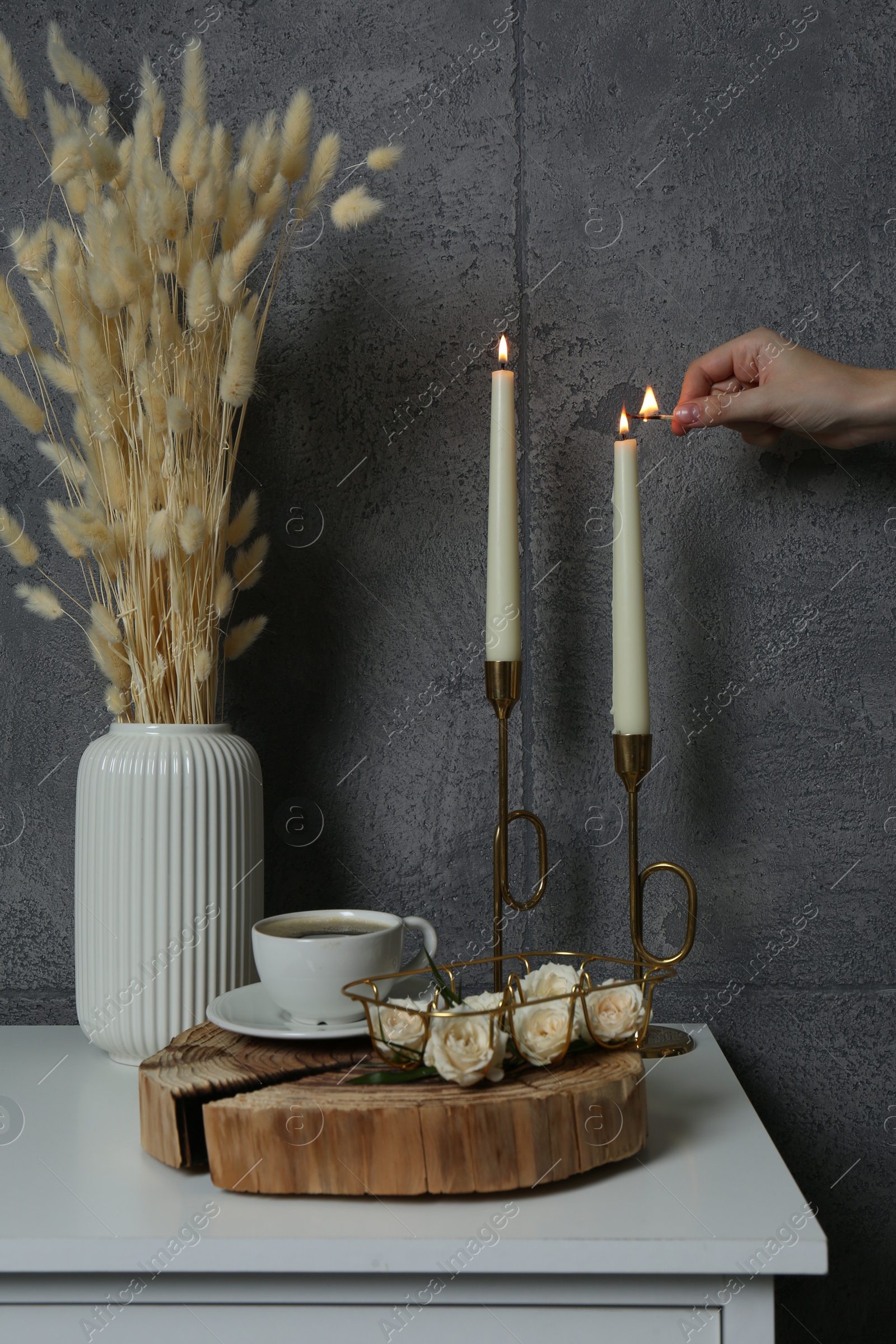 Photo of Woman lighting candle on table near grey wall indoors, closeup. Interior design