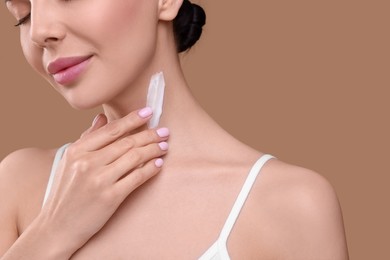 Beautiful woman with smear of body cream on her neck against light brown background, closeup