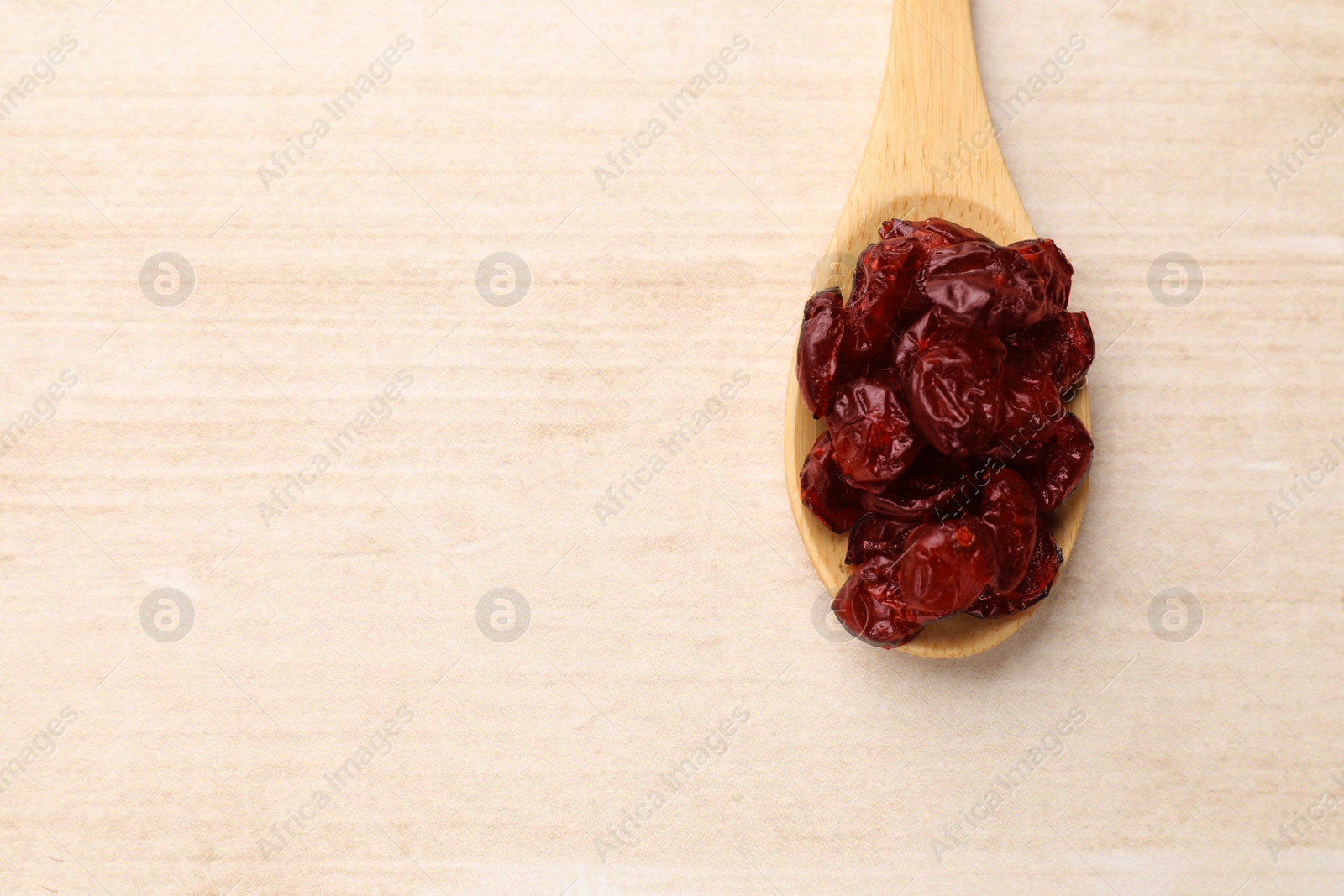 Photo of Spoon with dried cranberries on wooden table, top view. Space for text