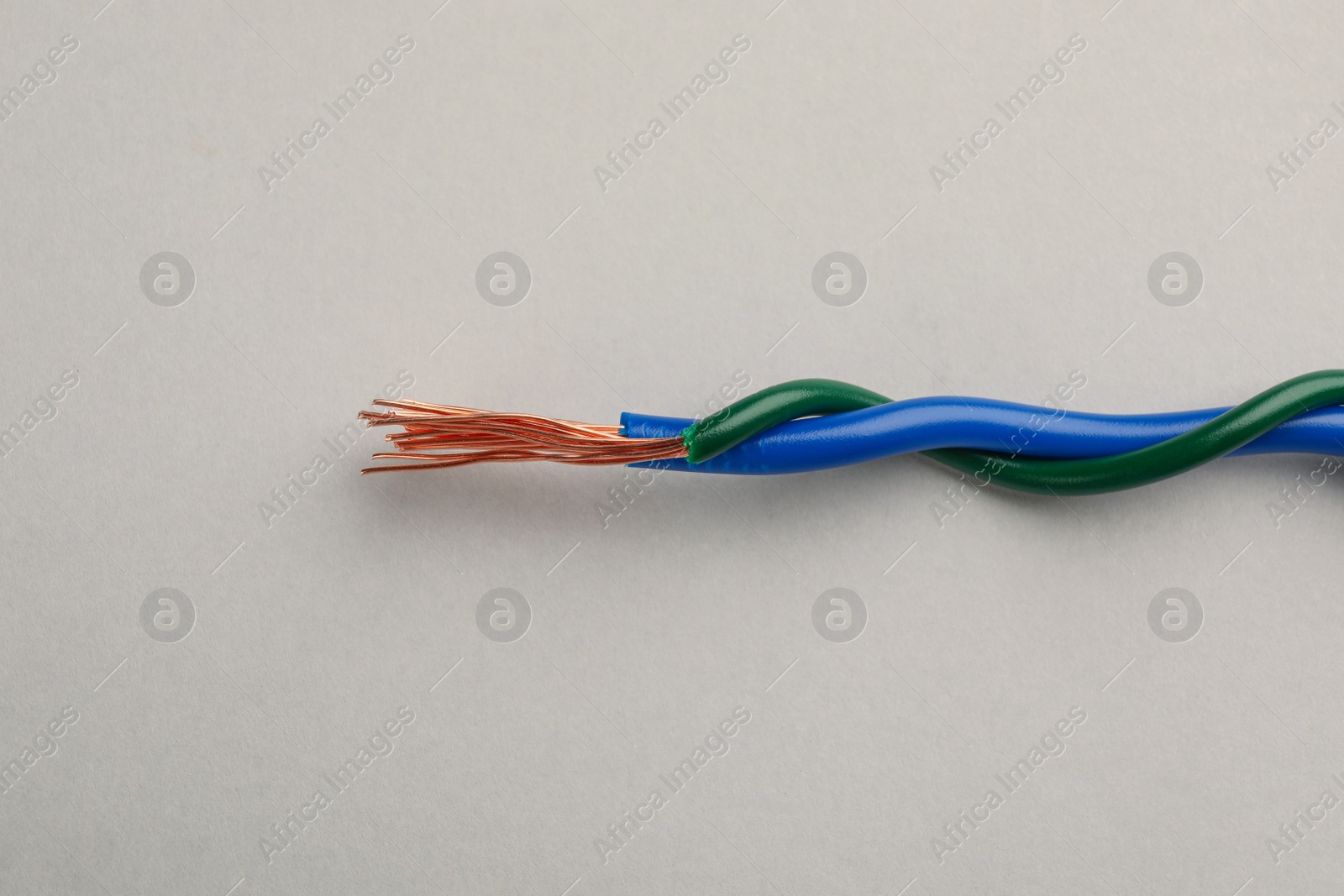 Photo of Two twisted electrical wires on light background, closeup