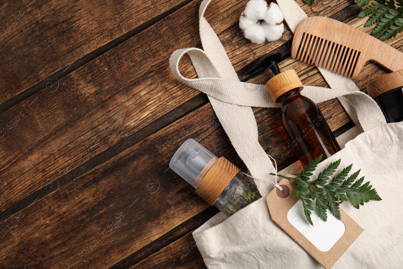 Photo of White cotton bag with eco friendly personal care products on wooden table, flat lay. Space for text