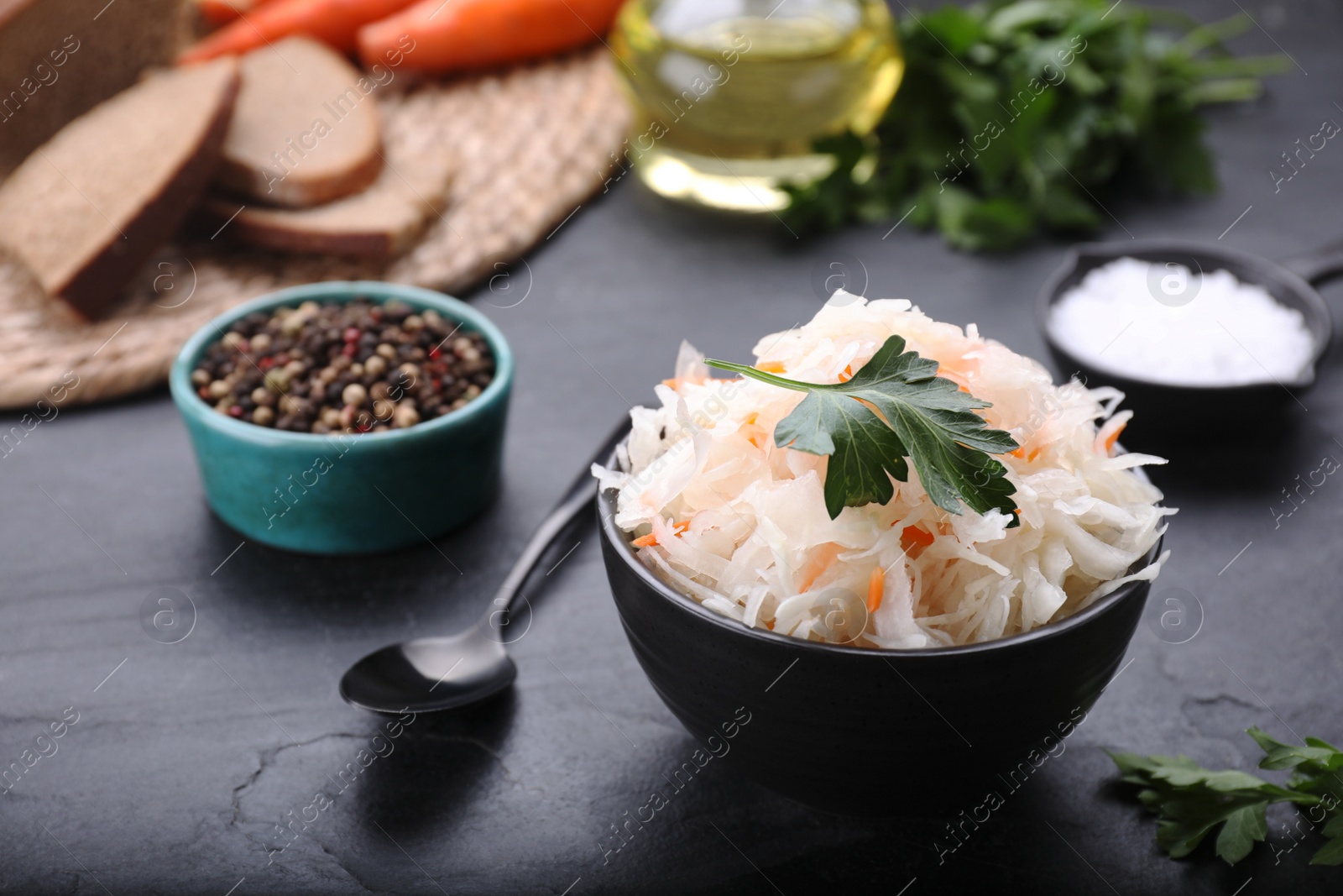 Photo of Bowl of tasty sauerkraut and ingredients on black table