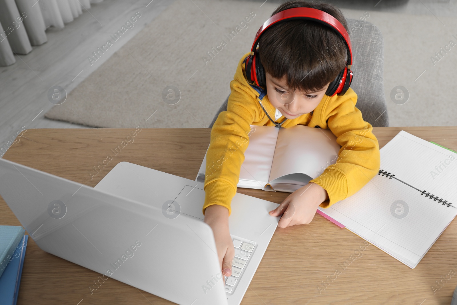 Photo of Cute little boy with modern laptop studying online at home. E-learning