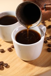 Pouring aromatic coffee from cezve into cup at wooden board, closeup