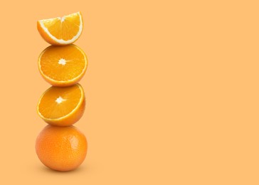 Stacked cut and whole oranges on light orange background, space for text