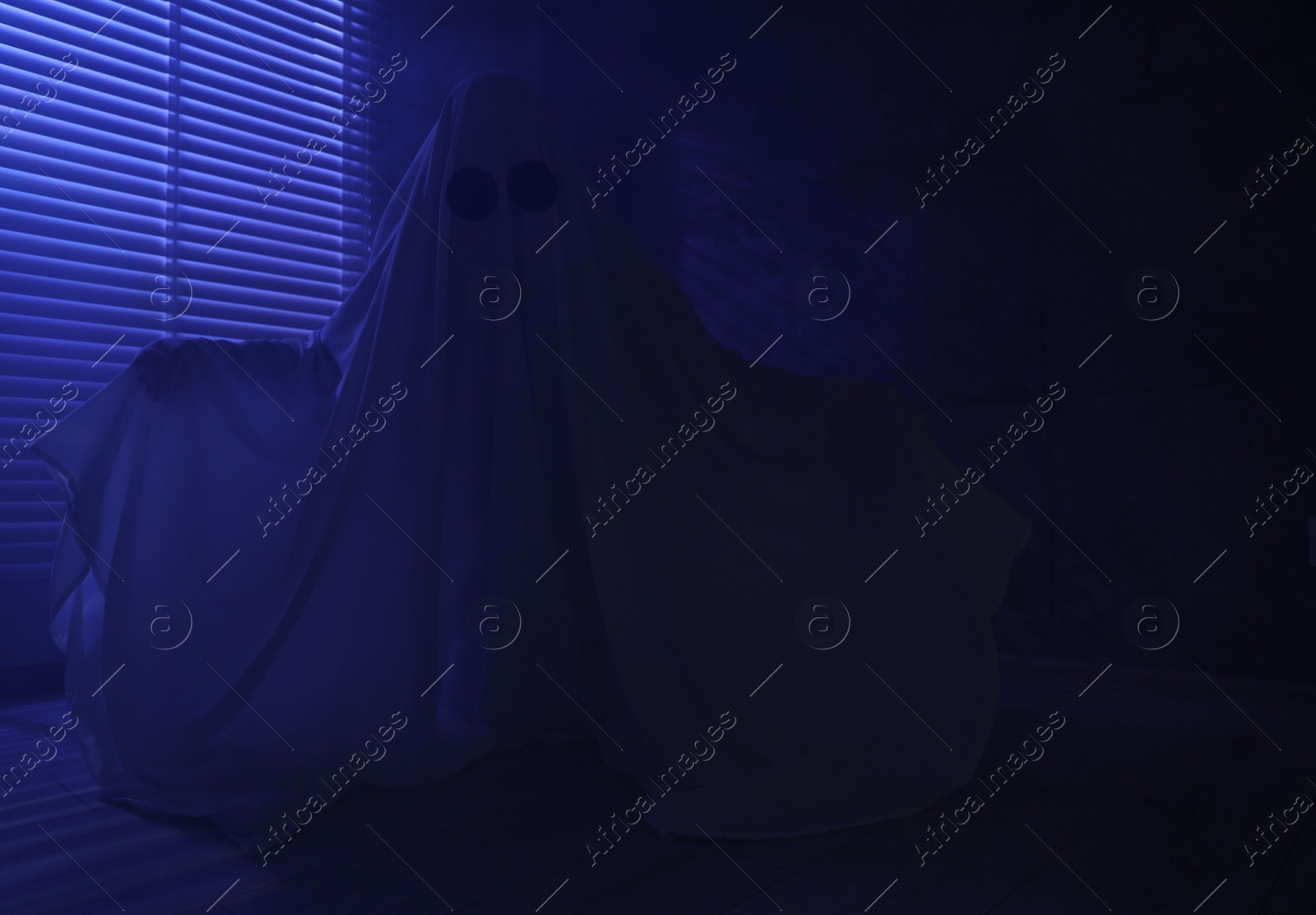 Photo of Creepy ghost. Woman covered with sheet near window in blue light