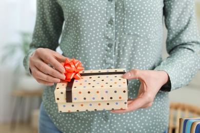Photo of Woman decorating gift box with bow indoors, closeup