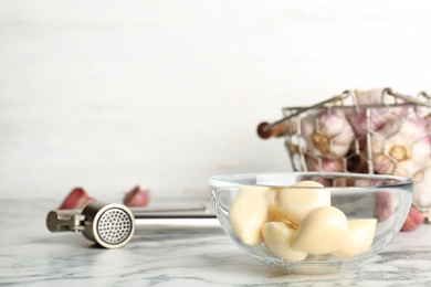 Photo of Garlic press and bowl with cloves on marble table